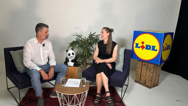 Zwei Interviewpartner führen ein engagiertes Gespräch über Artenschutz zwischen einem WWF-Panda und dem Lidl-Logo.