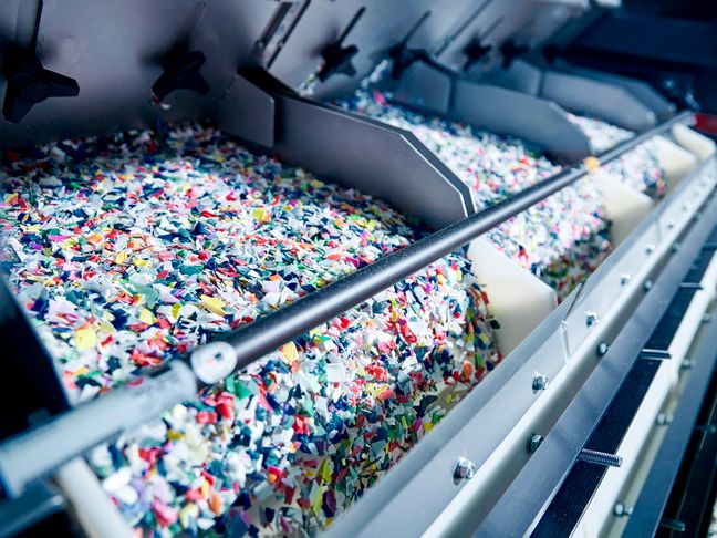 Buntes Kunststoff-Granulat läuft in einer Sortieranlage über Förderbänder für effizientes Ressourcen-Recycling.
