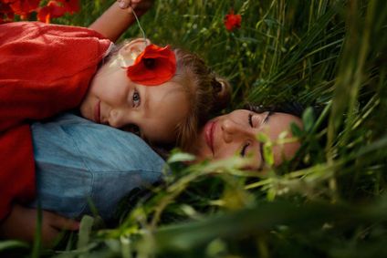 Una madre e sua figlia sdraiate in un prato di papaveri rossi.