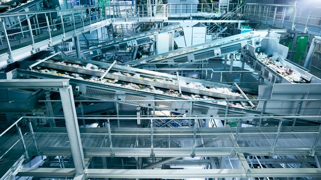 Zahlreiche Förderbänder transportieren Wertstoffe durch eine moderne, großflächige Recycling-Sortieranlage.