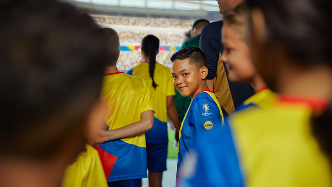 Ein lächelndes Einlaufkind im Lidl-Trikot steht im vollen Stadion-Tunnel und blickt beim Hinausgehen glücklich über die Schulter zurück.
