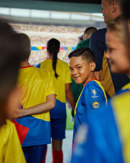 Ein lächelndes Einlaufkind im Lidl-Trikot steht im vollen Stadion-Tunnel und blickt beim Hinausgehen glücklich über die Schulter zurück.
