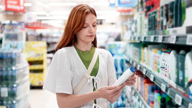 Kundin liest vor einem Supermarktregal die Hinweise eines Körperpflegeproduktes.