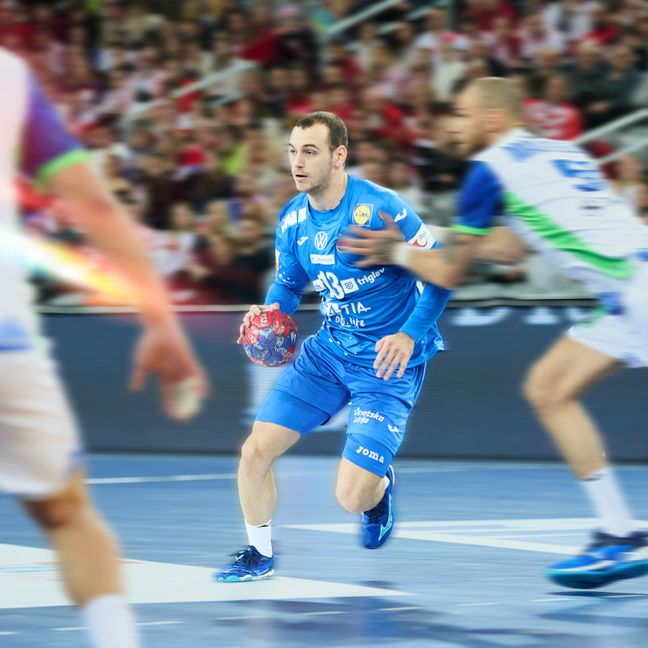 Hrvatski rukometaš u plavom dresu s brojem 13 vodi loptu u napadu tijekom utakmice.