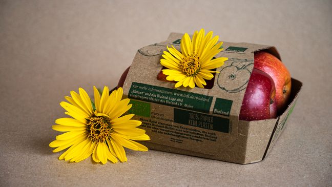 Rote Bioland-Äpfel in einer 100% papierbasierten Verpackung, dekoriert mit zwei strahlend gelben Blüten.