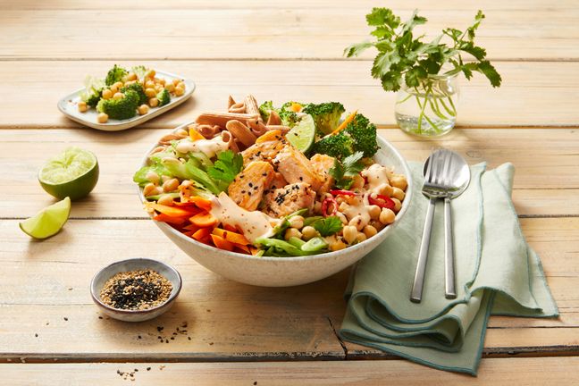 Frische Bowl mit Lachs, Kichererbsen und Brokkoli steht angerichtet auf einem Holztisch.