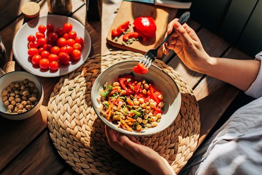 Alimentazione consapevole persona con piatto e forchetta che consuma pomodorini legumi e verdure varie