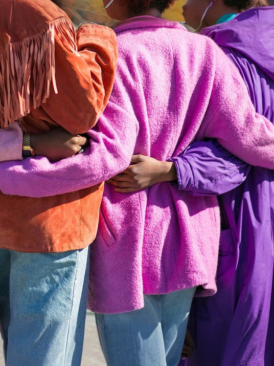 Nahaufnahme von drei eng eingehakten Personen in farbenfrohen Jacken von hinten als Symbol für gelebten Zusammenhalt.