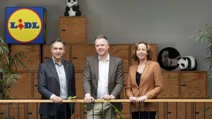Drei lächelnde Führungskräfte präsentieren die WWF Partnerschaft vor einem Lidl-Logo und dekorativen Pandabären.