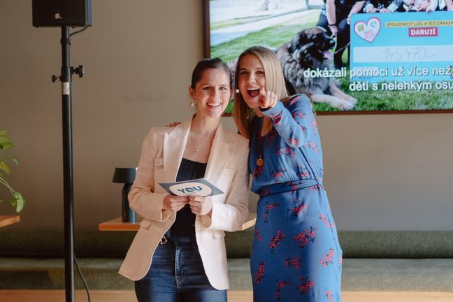 Zwei lachende Frauen, eine im blauen Kleid zeigt in Richtung Kamera, moderieren eine Lidl YOU Veranstaltung.