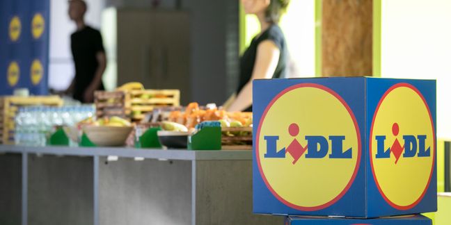 Kutije s Lidlovim logotipom u prvom planu te stol sa svježim voćem i osvježenjima na događaju u pozadini.