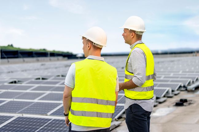 Zwei Techniker begutachten eine weitläufige Grünstrom-Solaranlage auf einem Flachdach unter klarem Himmel.