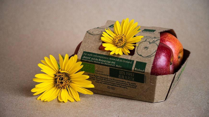 Rote Bioland-Äpfel in einer 100% papierbasierten Verpackung, dekoriert mit zwei strahlend gelben Blüten.