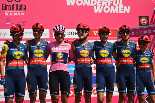 Das Lidl-Trek Team posiert Arm in Arm vor einer pinken Giro d'Italia Women Wand mit der Gesamtführenden in Rosa Trickot.