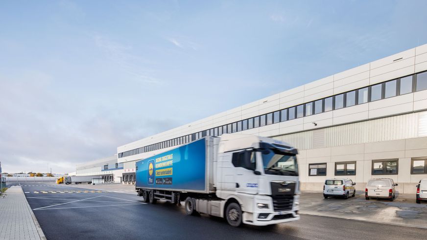 Lidl-Lkw fährt vor einem modernen Logistikzentrum auf dem Betriebsgelände.