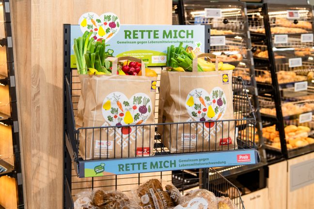 Zwei prall gefüllte Rettertüten mit Obst und Gemüse stehen verkaufsbereit im Regal für Lebensmittelrettung.