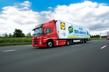 Ein roter Lidl E-Lkw mit einem weißen Auflieger, und der Aufschrift "100% elektrisch", fährt auf einer Autobahn.