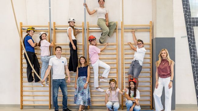 Grupa djece s speleološkim kacigama i voditelji poziraju na švedskim ljestvama u školskoj dvorani.