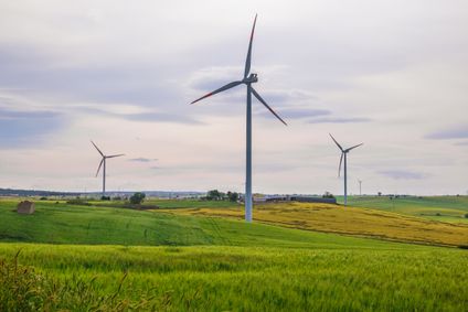 Moderne Windkraftanlagen zur Gewinnung von Grünstrom stehen verteilt auf weiten, grünen Feldern unter bewölktem Himmel.