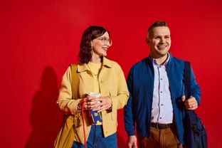 Two smiling Lidl employees in a modern business-casual look, posing in high spirits against a vibrant red background.
