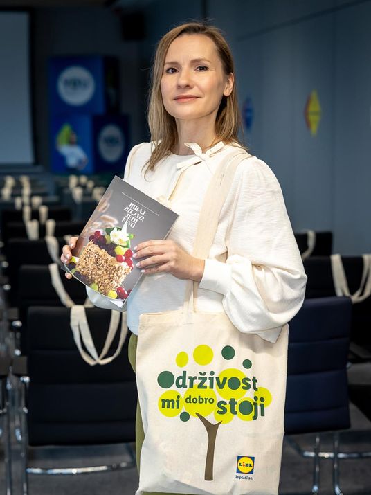 Eine Frau präsentiert lächelnd ein veganes Kochbuch und einen nachhaltigen Lidl Jutebeutel für bewusste pflanzliche Ernährung.