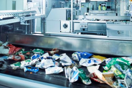 Kunststoffverpackungen laufen auf einem Förderband durch eine moderne Recyclinganlage.
