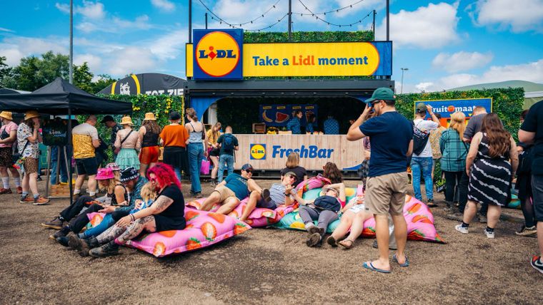 Festivalbesucher entspannen auf Sitzsäcken vor der mobilen Lidl FreshBar mit „Take a Lidl moment“-Schild.