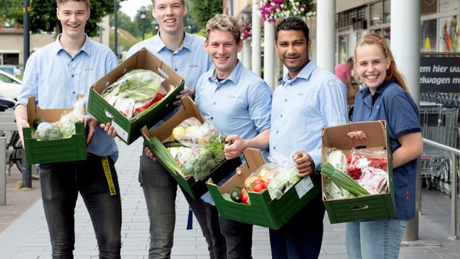 Fünf lächelnde Mitarbeiter präsentieren vor einer Filiale grüne Kisten voller Lebensmittelspenden.