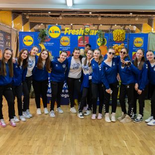 Mlada ženska sportska ekipa pozira u sportskoj dvorani ispred Lidlovog 'Fresh Bar' štanda.