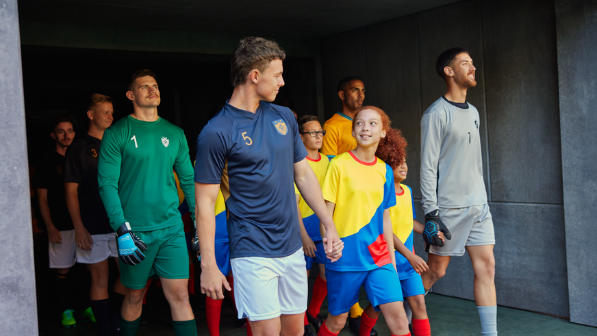A cheering young woman in a yellow jersey enthusiastically waving a large flag in a packed football stadium.