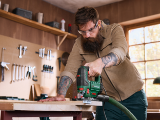 A craftsman wearing safety goggles guiding a PARKSIDE jigsaw through a wooden board.