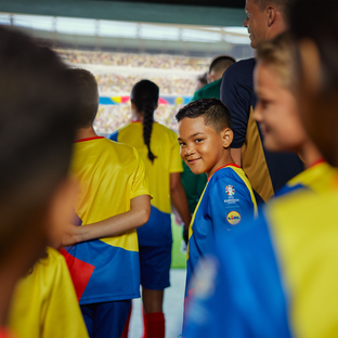 Dječak u dresu UEFA EURO 2024 s Lidl logotipom smiješi se na ulazu u stadion u sklopu dječjeg nogometnog tima.