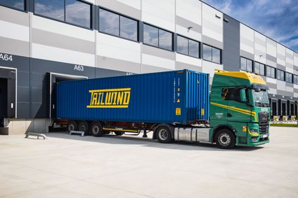 Ein grüner MAN-Lkw verlädt einen blauen Tailwind Container an der Logistikrampe eines modernen Warenlagers.
