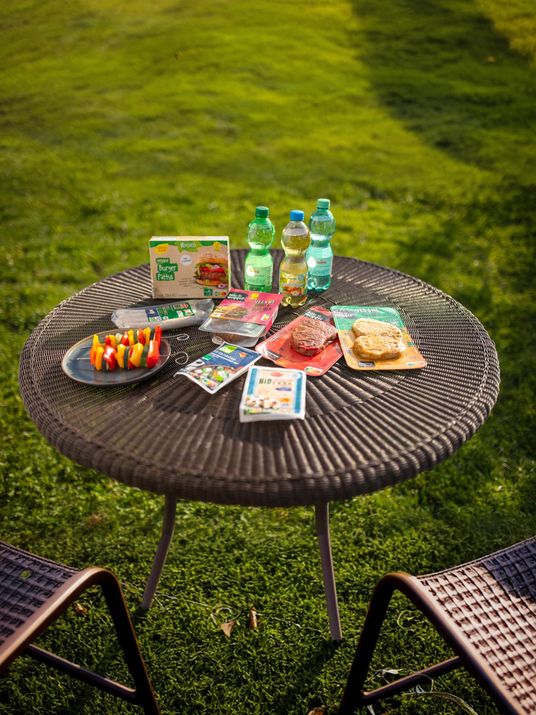 Verschiedene vegane Ersatzprodukte und Erfrischungsgetränke präsentieren auf einem Gartentisch vegane Produktvielfalt.