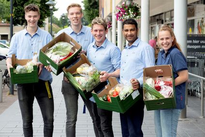 Fünf lächelnde Mitarbeiter präsentieren vor einer Filiale grüne Kisten voller Lebensmittelspenden.