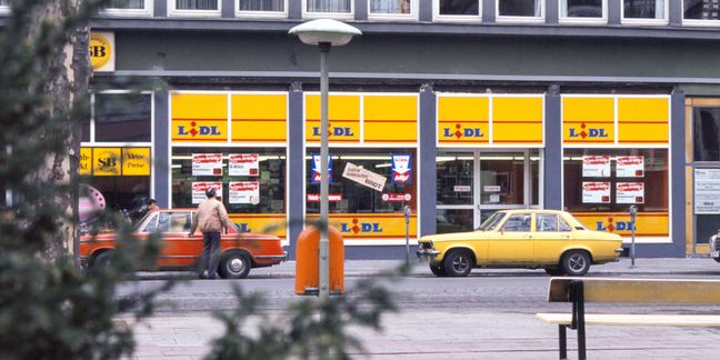 Eine historische Lidl-Filiale mit gelben Fensterfronten und zwei geparkten Oldtimern versprüht den Charme der 1970er-Jahre.