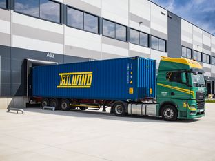 Ein grüner MAN-Lkw verlädt einen blauen Tailwind Container an der Logistikrampe eines modernen Warenlagers.