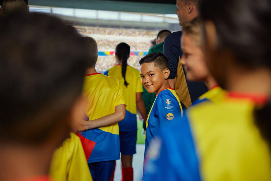 Dječak u dresu UEFA EURO 2024 s Lidl logotipom smiješi se na ulazu u stadion u sklopu dječjeg nogometnog tima.