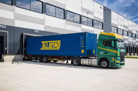 Ein grüner MAN-Lkw verlädt einen blauen Tailwind Container an der Logistikrampe eines modernen Warenlagers.