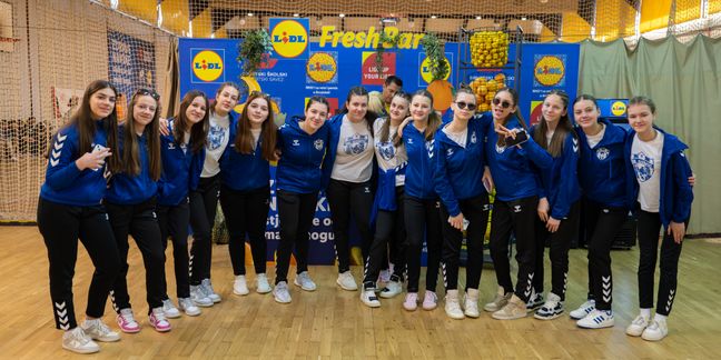 Mlada ženska sportska ekipa pozira u sportskoj dvorani ispred Lidlovog 'Fresh Bar' štanda.
