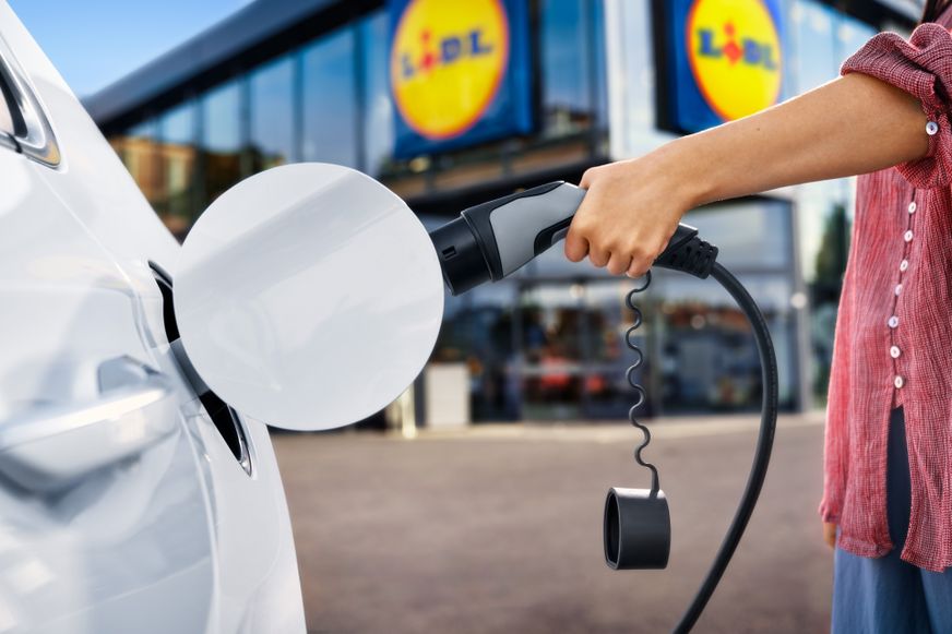 Osoba priključuje punjač u električni automobil ispred Lidlove trgovine.