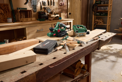 Parkside Werkzeuge wie Elektrohobel, Stichsäge und Stechbeitel liegen einsatzbereit auf einer rustikalen Werkbank aus Holz.