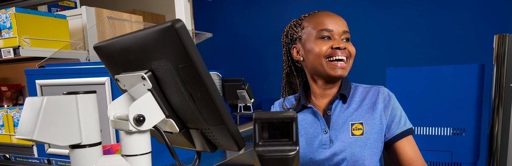 Eine herzlich lächelnde Lidl-Kassiererin scannt eine Honigmelone und verkörpert den schnellen und freundlichen Service an den Lidl Kassen.